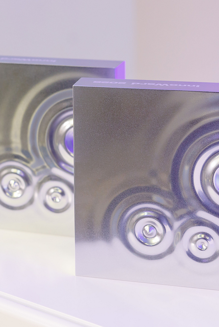 Vier quadratische Objekte mit glänzenden Oberflächen in verschiedenen Farbtönen (eins grün, drei silber) stehen auf einer weißen Fläche. Jedes Objekt zeigt kreisförmige Vertiefungen, die ein strukturiertes Design erzeugen. Die Anordnung betont das moderne und stilvolle Erscheinungsbild der Objekte.